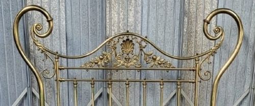 An ornate Victorian double brass bedstead featuring large outer scroll arms, a central shell casting, and vertical spindles on castors. View II