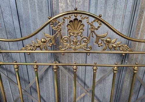 An ornate Victorian double brass bedstead featuring large outer scroll arms, a central shell casting, and vertical spindles on castors. View III
