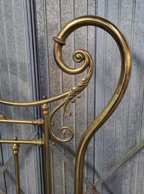 An ornate Victorian double brass bedstead featuring large outer scroll arms, a central shell casting, and vertical spindles on castors. View V