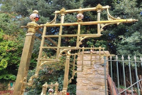 An antique Victorian king-size brass half tester bedstead featuring turned posts, decorative porcelain mounts, and an elevated canopy frame structure. View IV