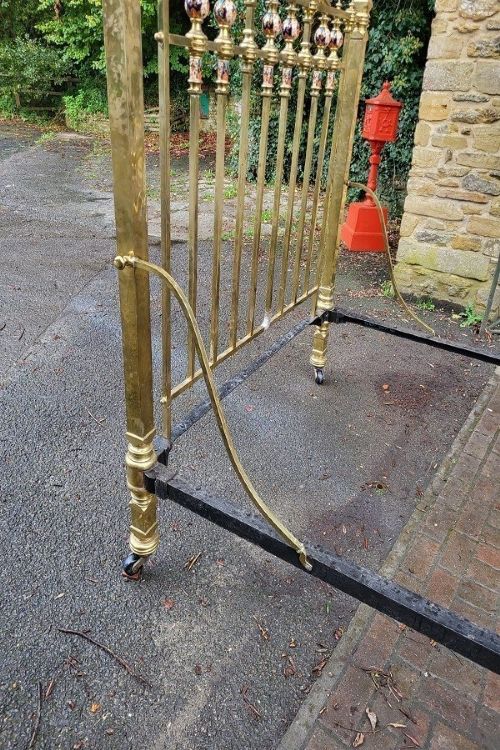 An antique Victorian king-size brass half tester bedstead featuring turned posts, decorative porcelain mounts, and an elevated canopy frame structure. View V