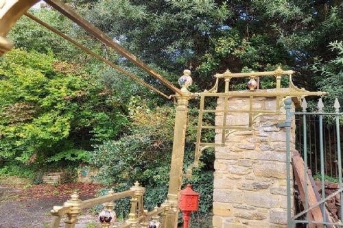 An antique Victorian king-size brass half tester bedstead featuring turned posts, decorative porcelain mounts, and an elevated canopy frame structure. View X