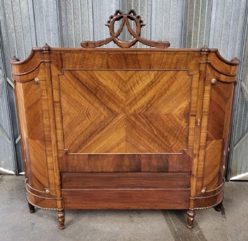 fig 1. A 19th-century French walnut bedstead featuring geometric quarter-veneered panels, fluted side posts, turned feet, and a carved ribbon top crest.