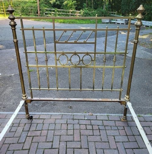fig 1. An antique king size brass bedstead featuring geometric rod spindles, circular motifs, urn finials, and castors.