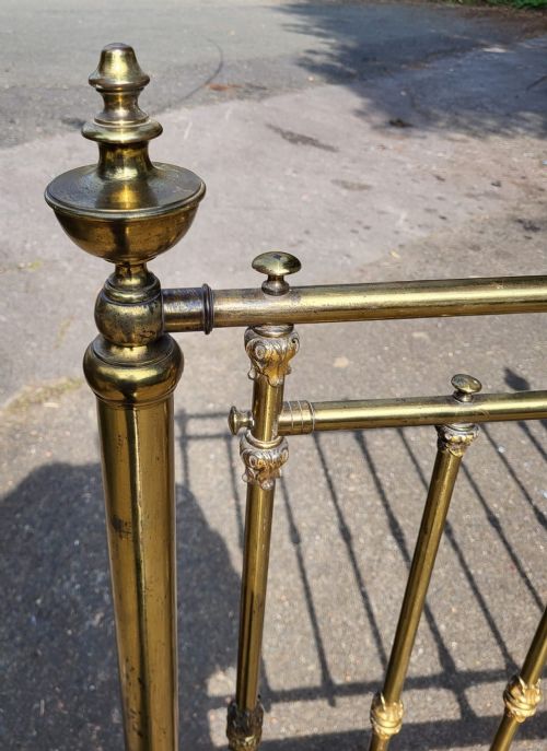 A Victorian small double brass bedstead featuring vertical spindled headboard and footboard panels with turned finials and green painted cast iron rails. View II