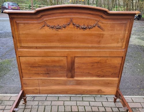 A late nineteenth-century French carved walnut bedstead with a panelled headboard, low footboard, and carved floral garlands. View II