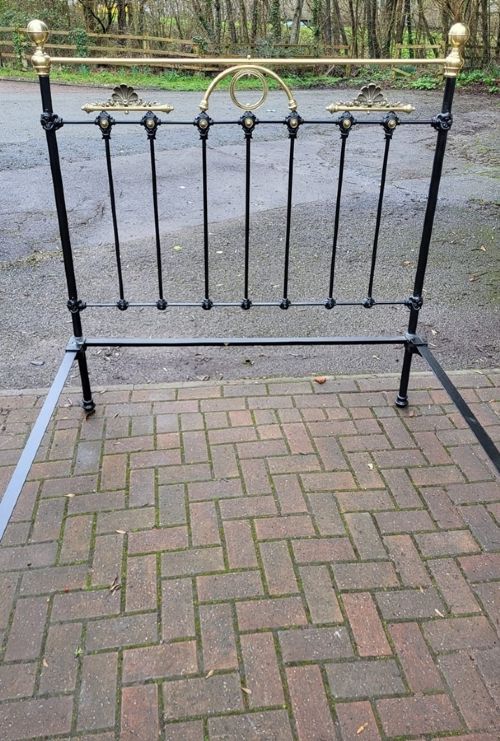 A Victorian double bedstead constructed from black-painted iron vertical spindles with top brass rails, brass finials, and central ornamental brass motifs. View II