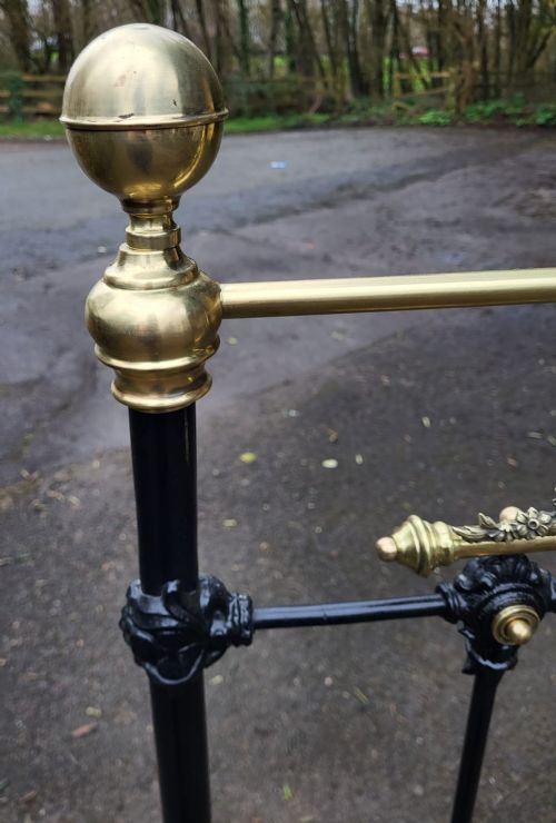 A Victorian double bedstead constructed from black-painted iron vertical spindles with top brass rails, brass finials, and central ornamental brass motifs. View V