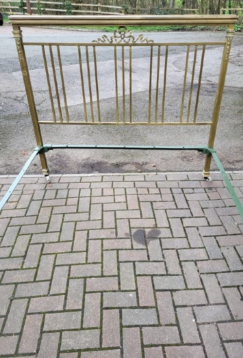 A Victorian king size brass bedstead featuring vertical spindles, an ornamental ribbon swag motif, and brass tubular frames on castors. View II