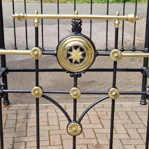 A Victorian king size black cast iron and polished brass bedstead featuring decorative central brass medallion detailing and top rails. View III