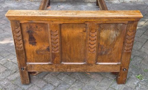 An Edwardian carved oak bedstead featuring a high panelled headboard with carved motifs and a matching lower footboard. View II