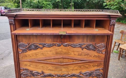A 19th-century flame mahogany secretaire a abattant featuring carved scrollwork, diamond veneer patterns, lower cupboards with rosette medallions, and a brass gallery top. View II