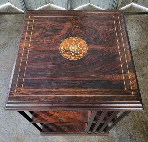 An Edwardian inlaid rosewood revolving bookcase featuring a square top with a central floral marquetry medallion, double stringing border, vertical side slats, and castors at the base. View II