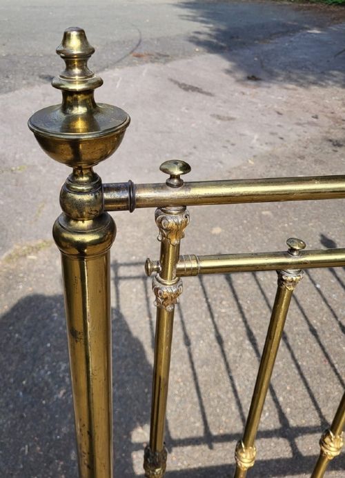 A Victorian small double brass bedstead featuring vertical brass spindles, decorative finials, green painted iron side rails, and white ceramic castors. View II
