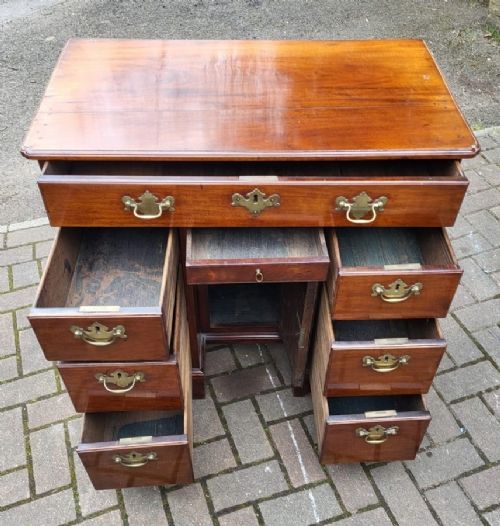 A Georgian mahogany kneehole writing desk with brass handles, multiple side drawers, and a recessed central cupboard raised on bracket feet. View II
