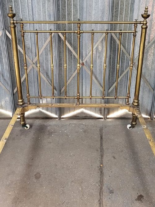 A Victorian brass small double bedstead featuring vertical spindles, decorative brass finials, side rails, and ceramic castors. View II