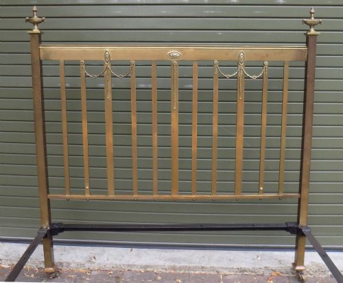 fig 1. An antique Victorian brass bedstead with decorative urn finials, vertical spindles, ribbon swags, and castors.