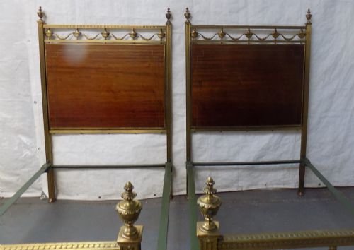 fig 1. A pair of late Victorian brass-framed twin bedsteads featuring polished brass rails, top drapery swags, urn finials, and central mahogany timber panels with decorative brass plaques.