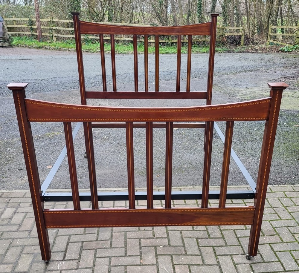 An Edwardian double bedstead crafted from polished mahogany with vertical slatted panels and delicate line inlay across the headboard and footboard.