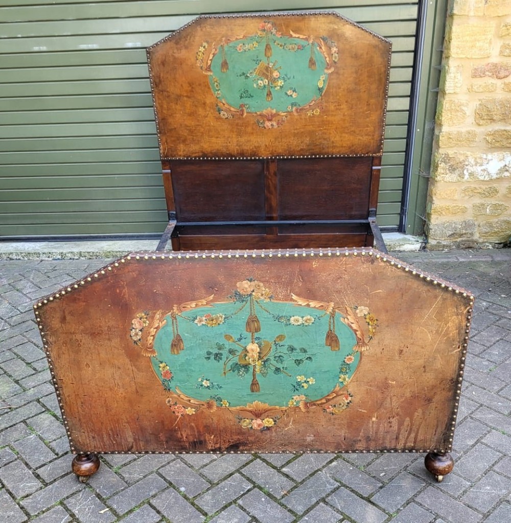 A Victorian Dutch style small double bedstead featuring a mahogany frame with hand painted floral cartouches on leather panels trimmed with brass studs.