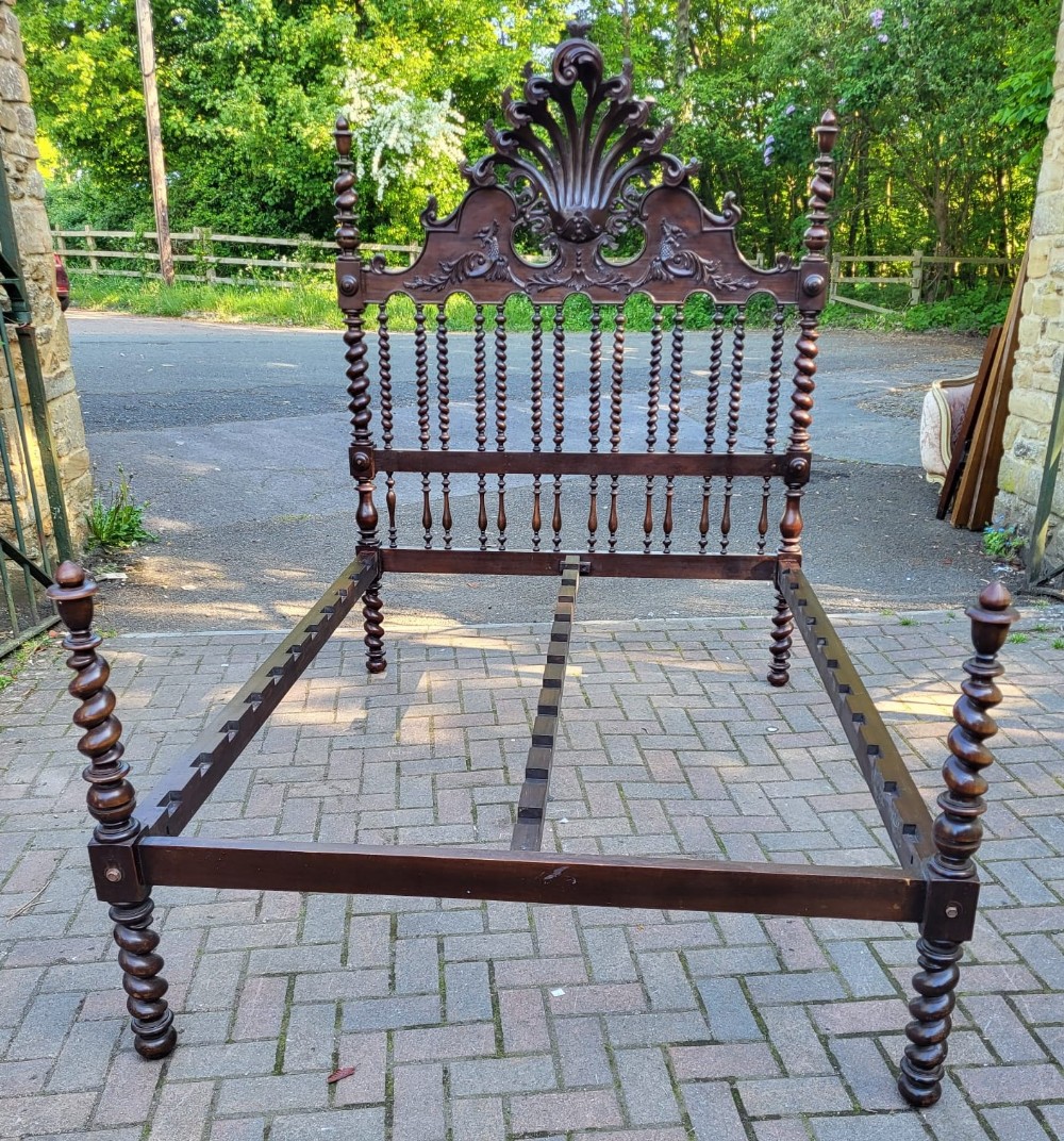 A 19th-century Portuguese double bedstead crafted from dark wood featuring ornate carved shell cresting and barley twist posts.