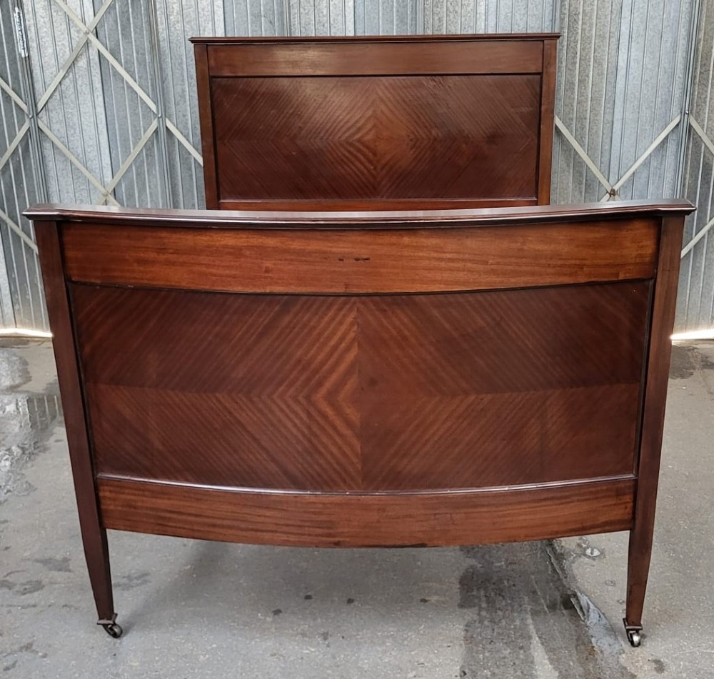 An Edwardian mahogany double bedstead featuring a curved footboard with chevron parquetry veneering, tapered legs, and castors.