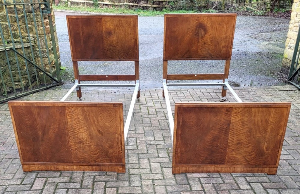 A pair of matching Edwardian single bedsteads crafted from figured walnut with rectangular panelled headboards and footboards.