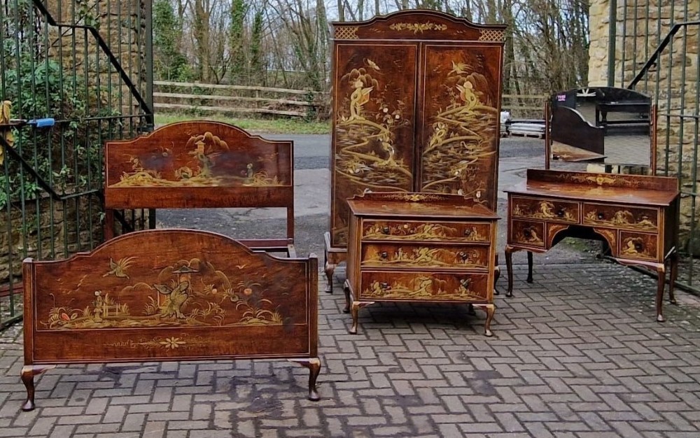 A four-piece Edwardian walnut bedroom suite decorated with gold Chinoiserie scenes, consisting of a bedstead, tall wardrobe, dressing table, and chest of drawers.