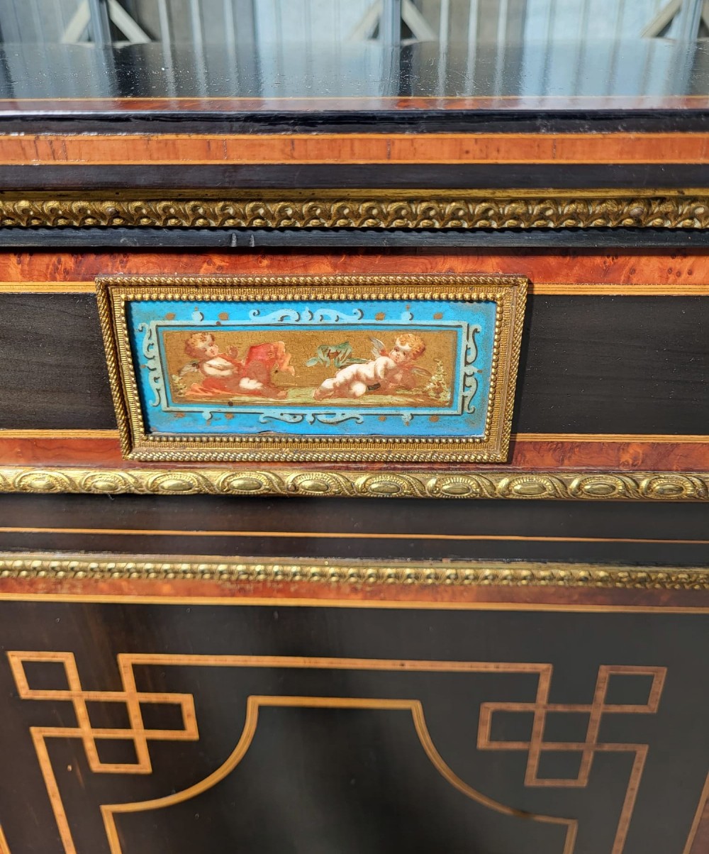 A Victorian ebonised three-door side cabinet featuring gilt-ormolu mounts, geometric marquetry, inlaid porcelain plaques, and a central glazed display door. View V