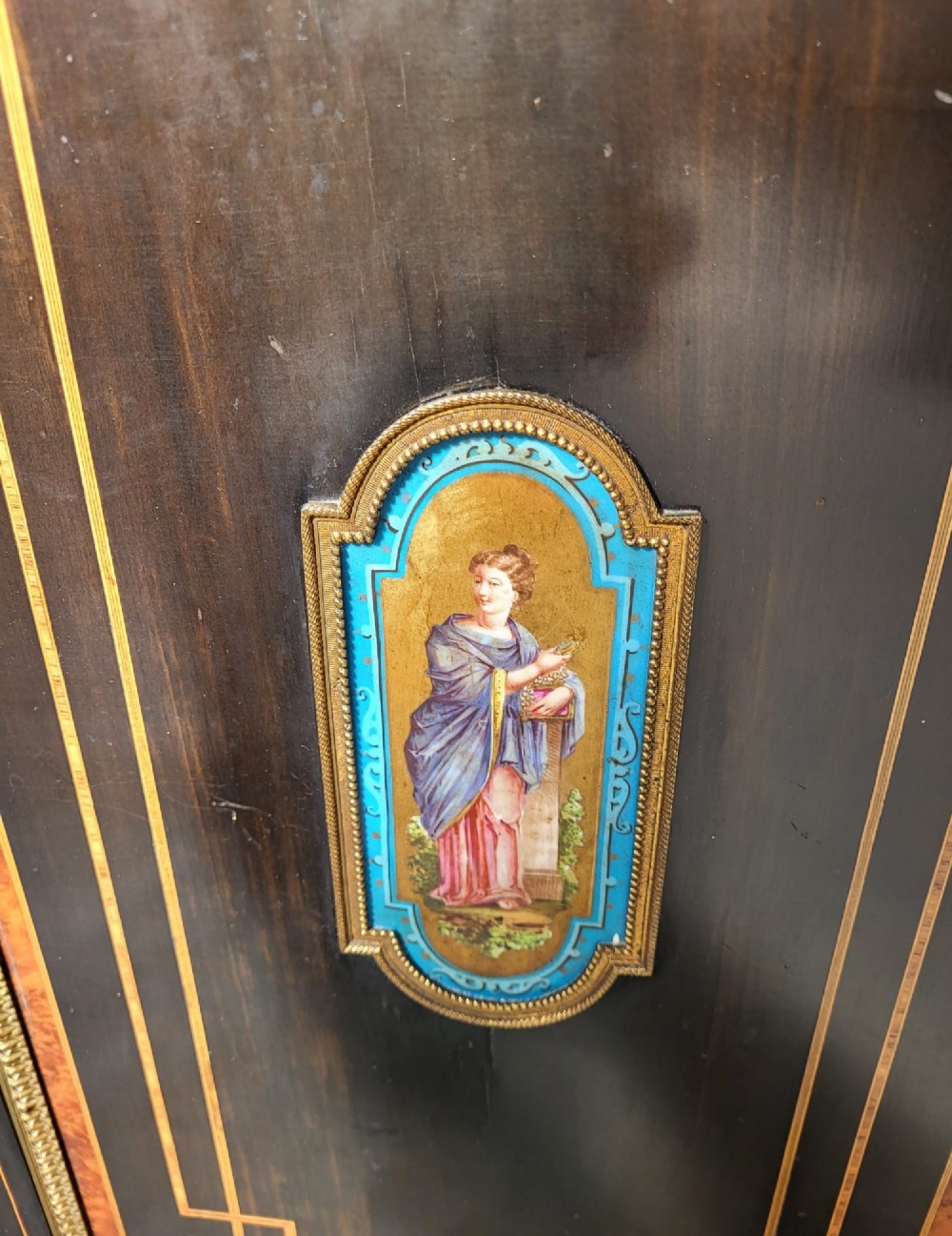 A Victorian ebonised three-door side cabinet featuring gilt-ormolu mounts, geometric marquetry, inlaid porcelain plaques, and a central glazed display door. View VI