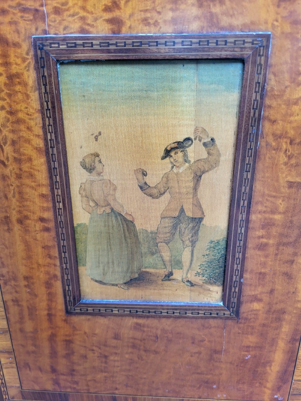 A golden satinwood side cabinet featuring painted figurative door panels, marquetry inlay swags, a top drawer with brass handles, and square tapered legs. View VI