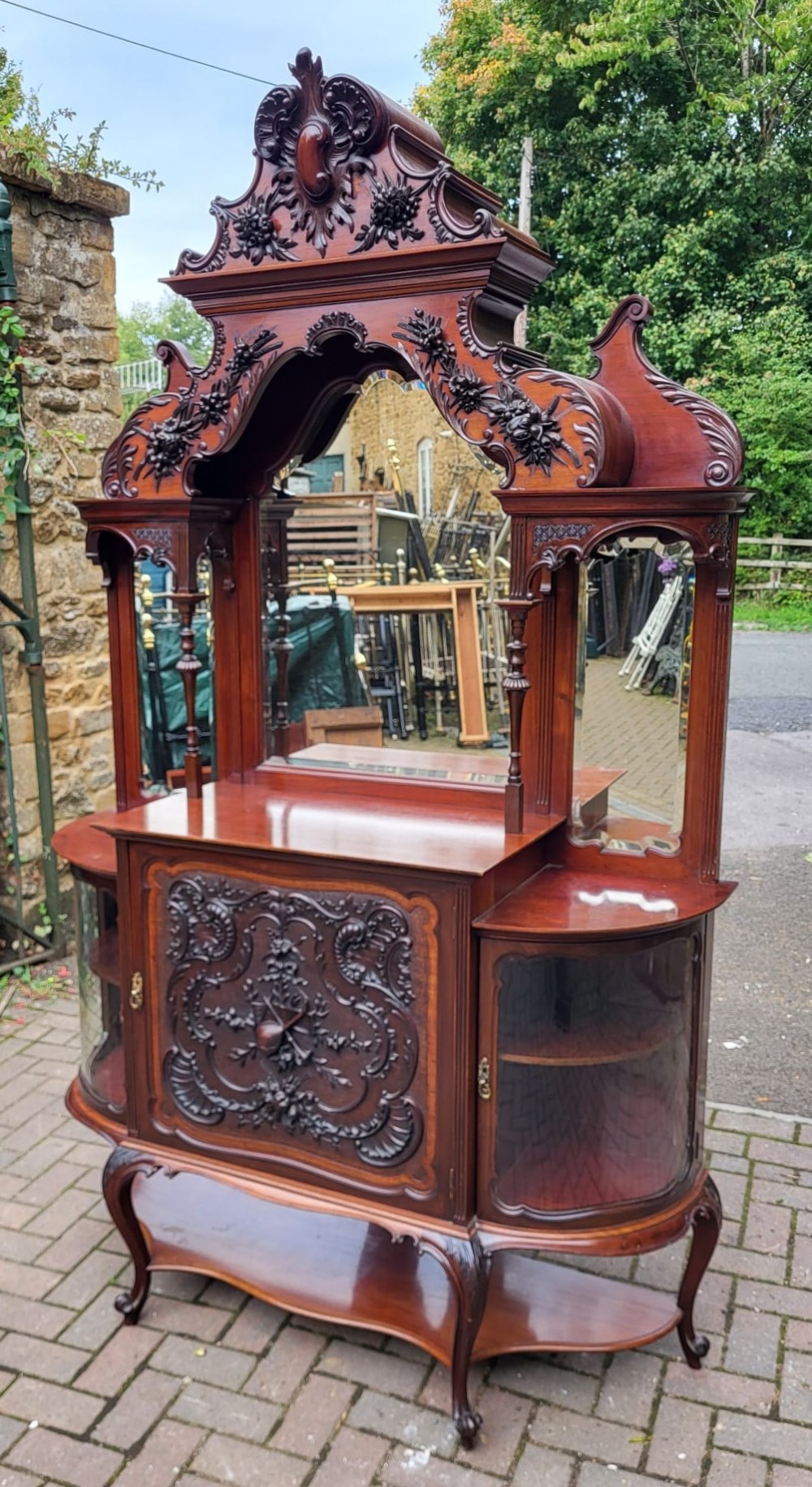An ornate Victorian carved mahogany mirror-back cabinet featuring a central carved panel door, curved glazed side displays, top mirrors, and cabriole legs. View II