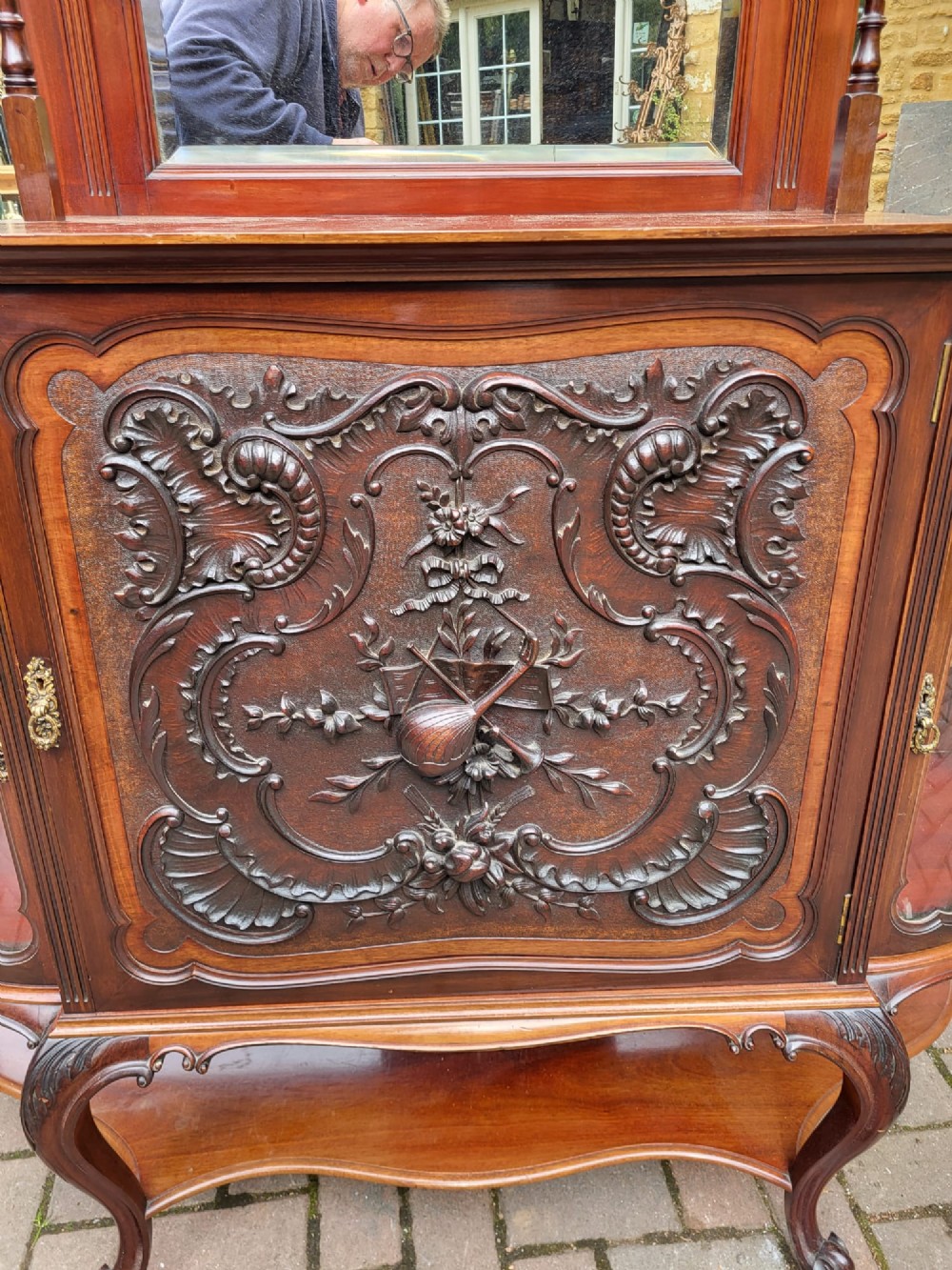 An ornate Victorian carved mahogany mirror-back cabinet featuring a central carved panel door, curved glazed side displays, top mirrors, and cabriole legs. View III