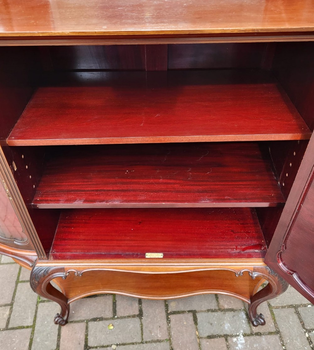 An ornate Victorian carved mahogany mirror-back cabinet featuring a central carved panel door, curved glazed side displays, top mirrors, and cabriole legs. View VI