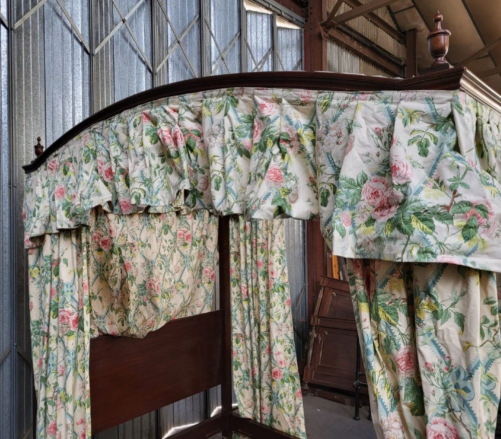 An Edwardian king size mahogany four poster bedstead featuring turned finials, a plain headboard panel, and floral textile curtains. View IV