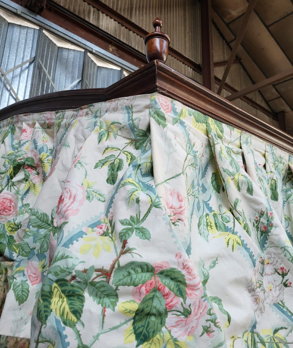 An Edwardian king size mahogany four poster bedstead featuring turned finials, a plain headboard panel, and floral textile curtains. View V