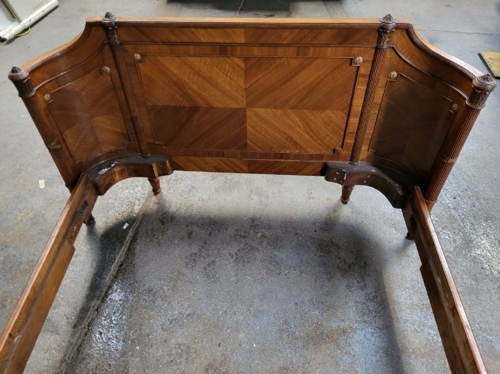 A 19th-century French walnut bedstead featuring geometric quarter-veneered panels, fluted side posts, turned feet, and a carved ribbon top crest. View V