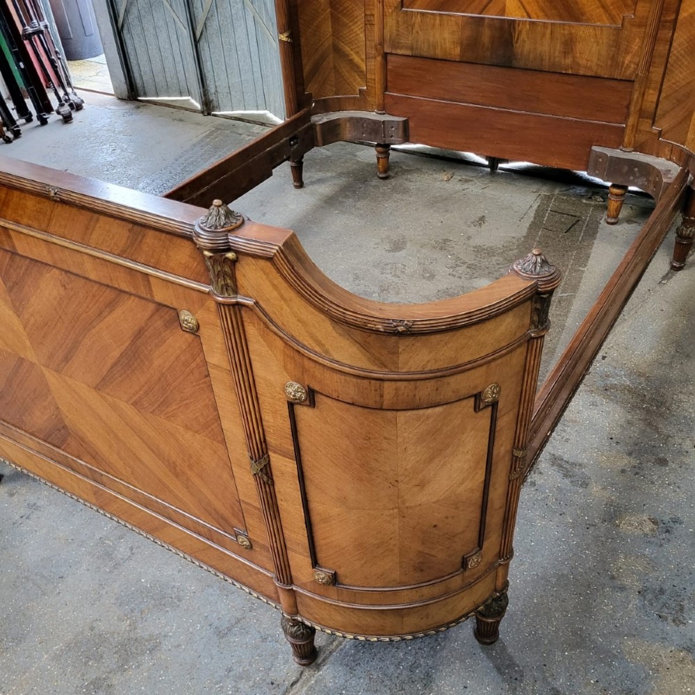 A 19th-century French walnut bedstead featuring geometric quarter-veneered panels, fluted side posts, turned feet, and a carved ribbon top crest. View VI