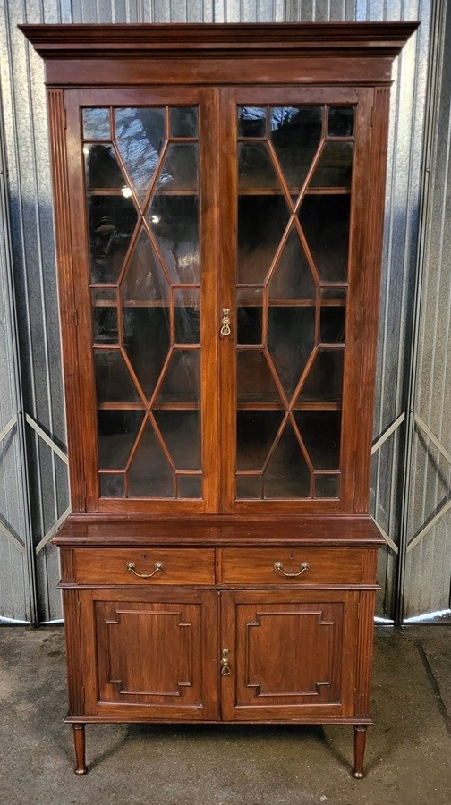 An Edwardian mahogany glazed bookcase featuring geometric astragal glass upper doors above two drawers and a panelled two-door base cabinet.