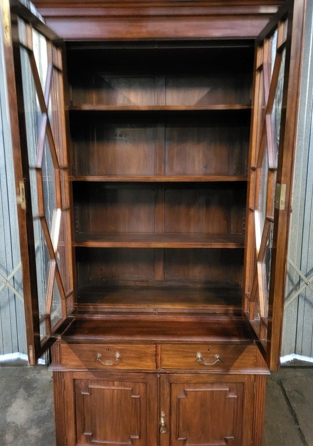 An Edwardian mahogany glazed bookcase featuring geometric astragal glass upper doors above two drawers and a panelled two-door base cabinet. View II