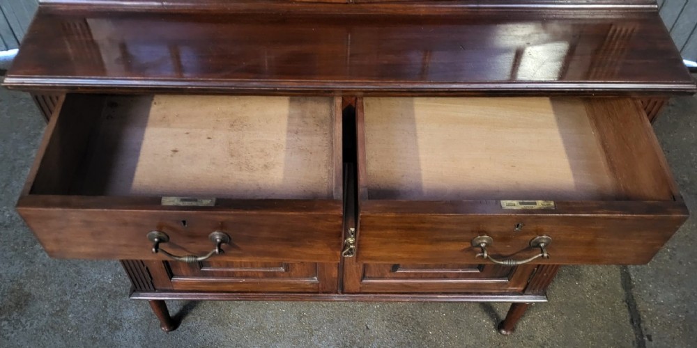 An Edwardian mahogany glazed bookcase featuring geometric astragal glass upper doors above two drawers and a panelled two-door base cabinet. View IV
