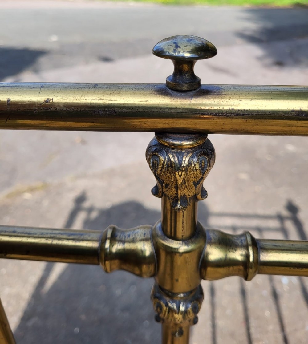 A Victorian small double brass bedstead featuring vertical spindled headboard and footboard panels with turned finials and green painted cast iron rails. View III