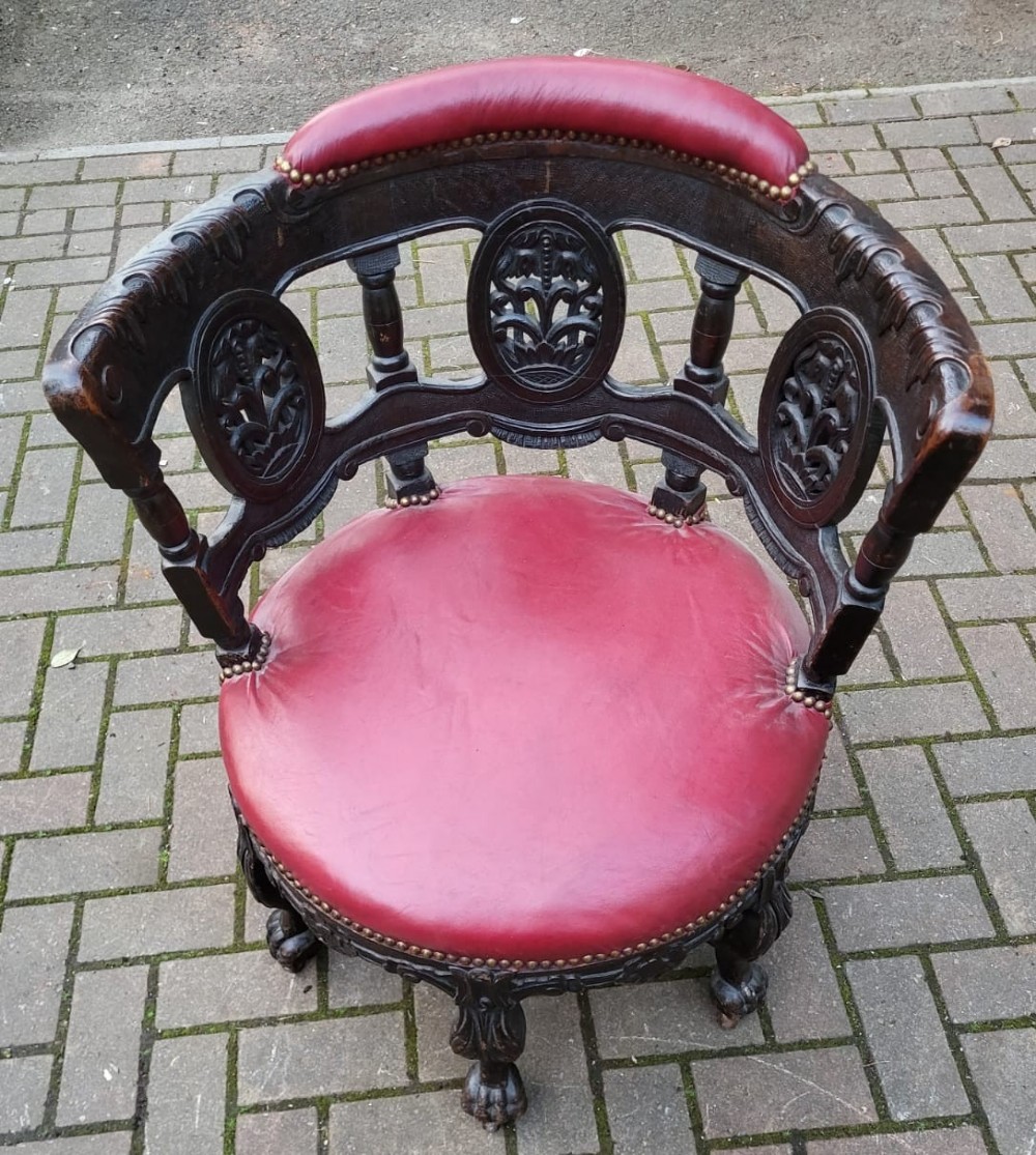 A Victorian carved oak burgomaster chair featuring a red leather circular seat, brass studding, and three oval carved back panels.