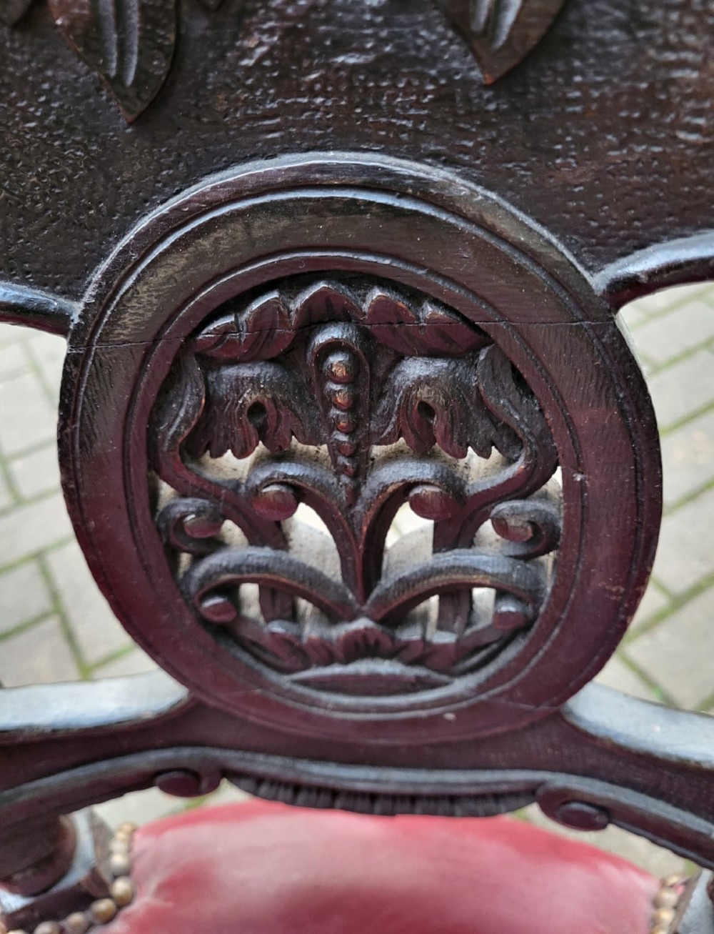 A Victorian carved oak burgomaster chair featuring a red leather circular seat, brass studding, and three oval carved back panels. View II
