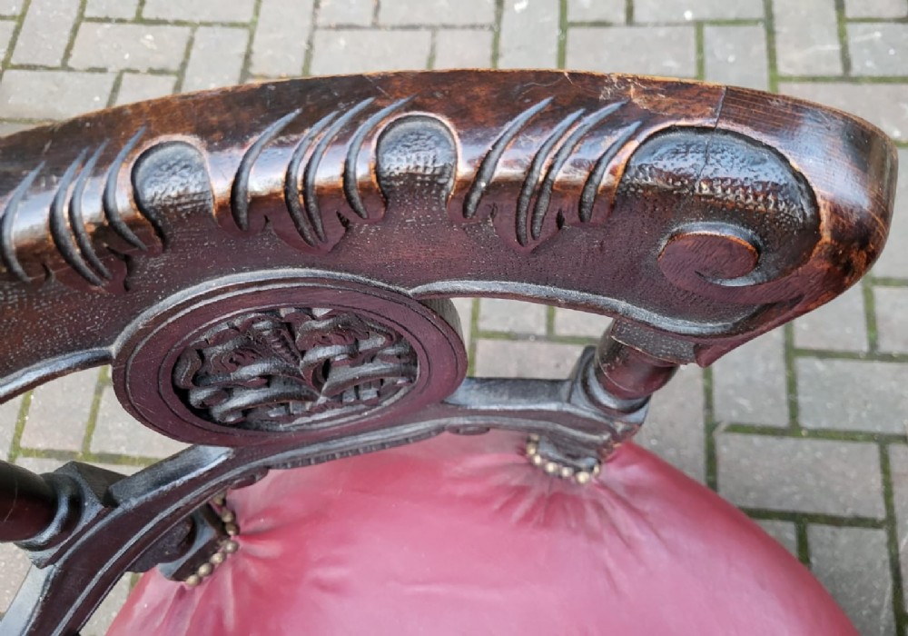 A Victorian carved oak burgomaster chair featuring a red leather circular seat, brass studding, and three oval carved back panels. View III