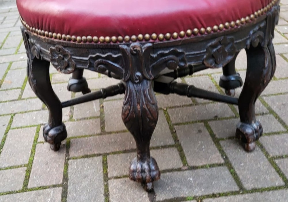 A Victorian carved oak burgomaster chair featuring a red leather circular seat, brass studding, and three oval carved back panels. View IV