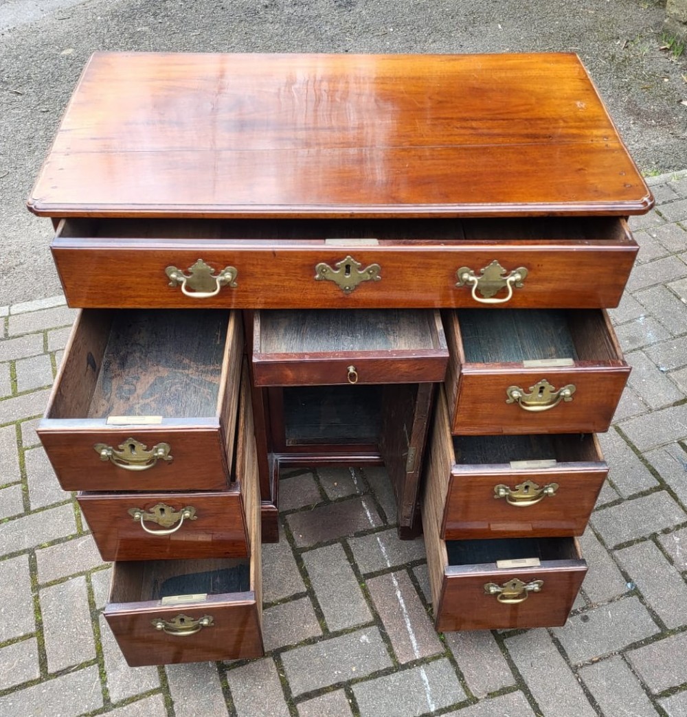 A Georgian mahogany kneehole desk featuring a long top drawer over six side drawers and a recessed central cupboard with brass handles and bracket feet. View II