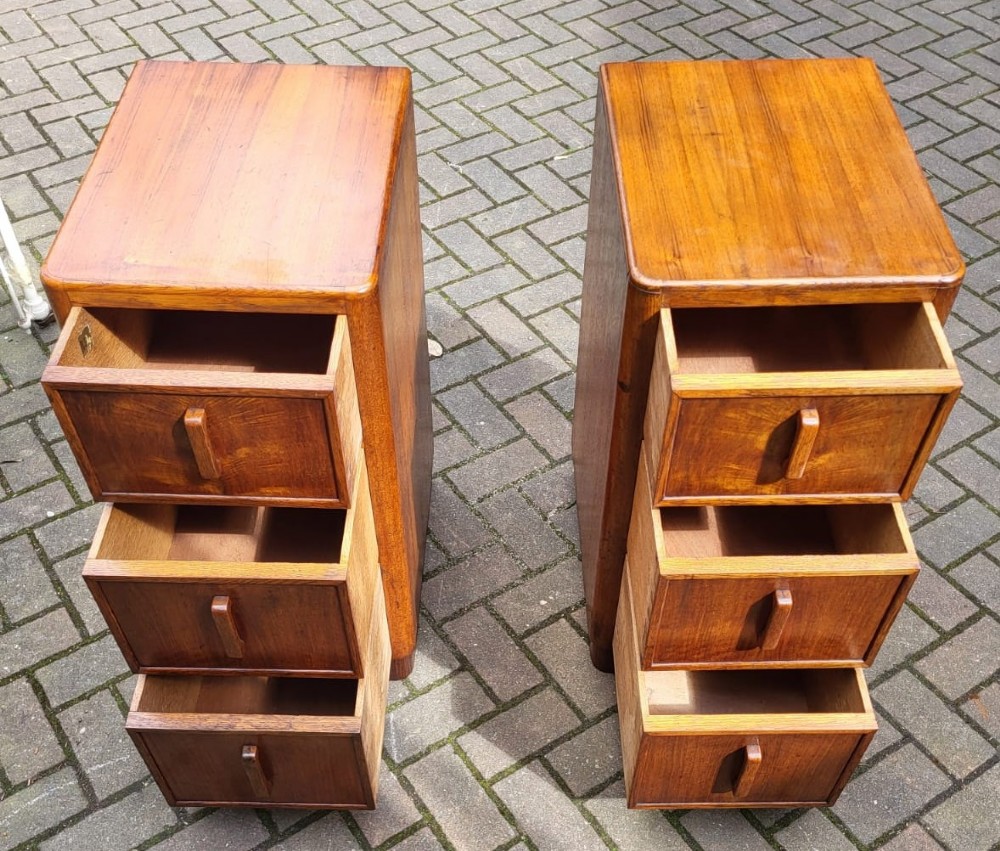 A matching pair of tall Art Deco oak bedside cabinets, each featuring three drawers with vertical wooden handles and curved upper corners. View II