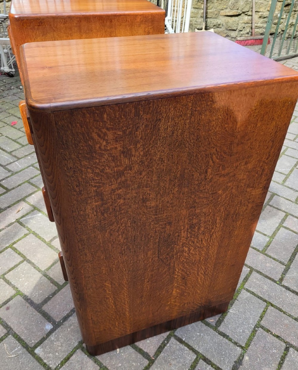 A matching pair of tall Art Deco oak bedside cabinets, each featuring three drawers with vertical wooden handles and curved upper corners. View III