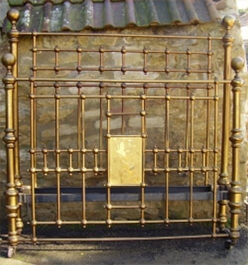 A Victorian king-size brass bedstead featuring decorative vertical spindles, turned ball finials, and a central engraved brass plaque.